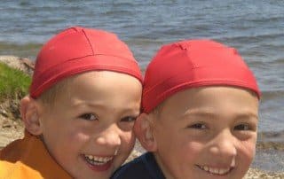twin boys on the beach wearing matching red jr. sun protective swim cap