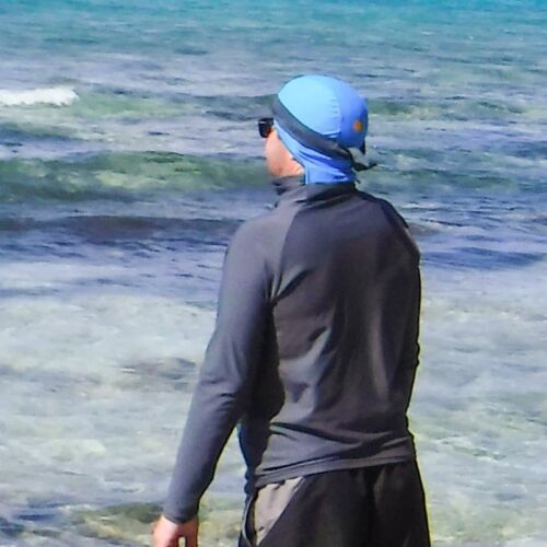 a man walking on the beach wearing sun protective rushguard shirt dark gray