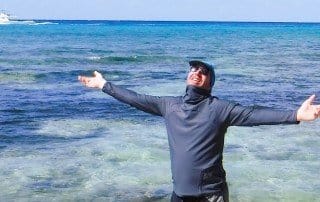 a man walking on the beach wearing sun protective rushguard shirt dark gray
