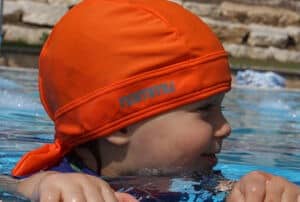 toddler with orange nammu sun protective swim hast at the pool