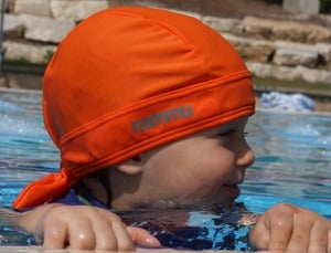 toddler with orange nammu sun protective swim hast at the pool